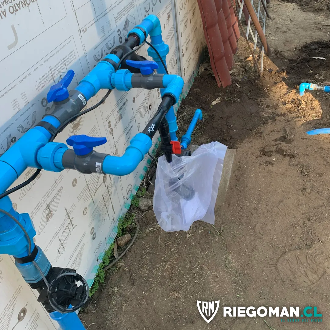 Conexiones hidráulicas de PVC con llaves de paso y válvula de riego junto a una vivienda